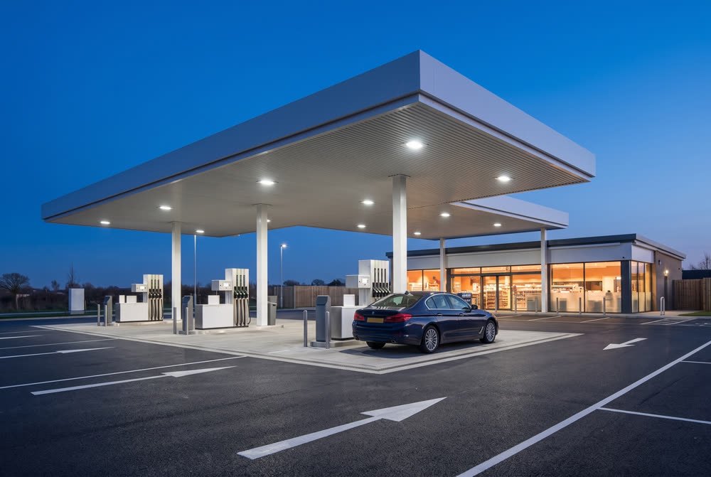 The same petrol forecourt at night with the canopy lit