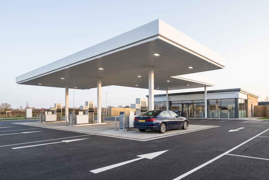 A petrol station forecourt at dusk with cars at the pumps
